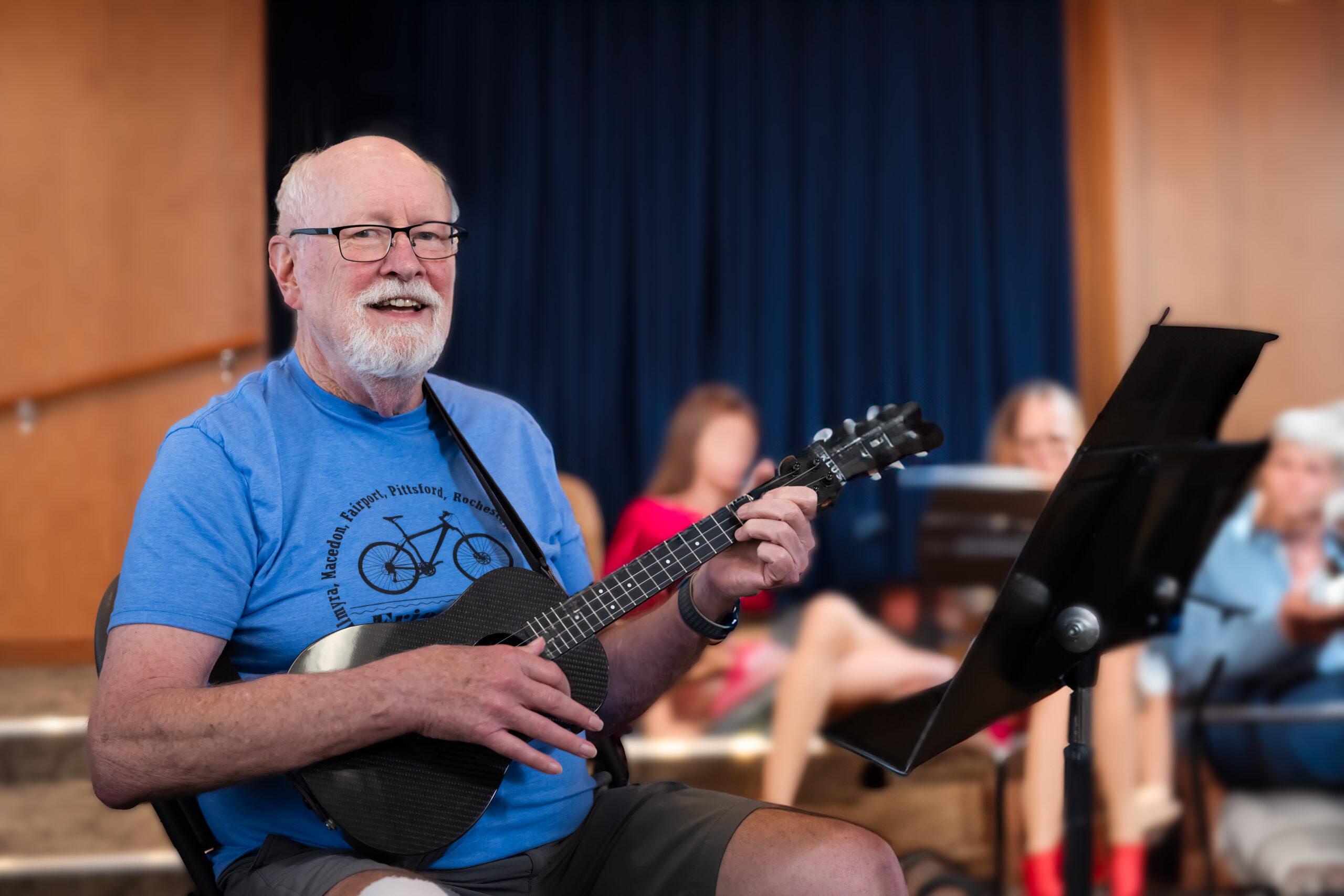 A man plays a ukulele and looks at the camera.