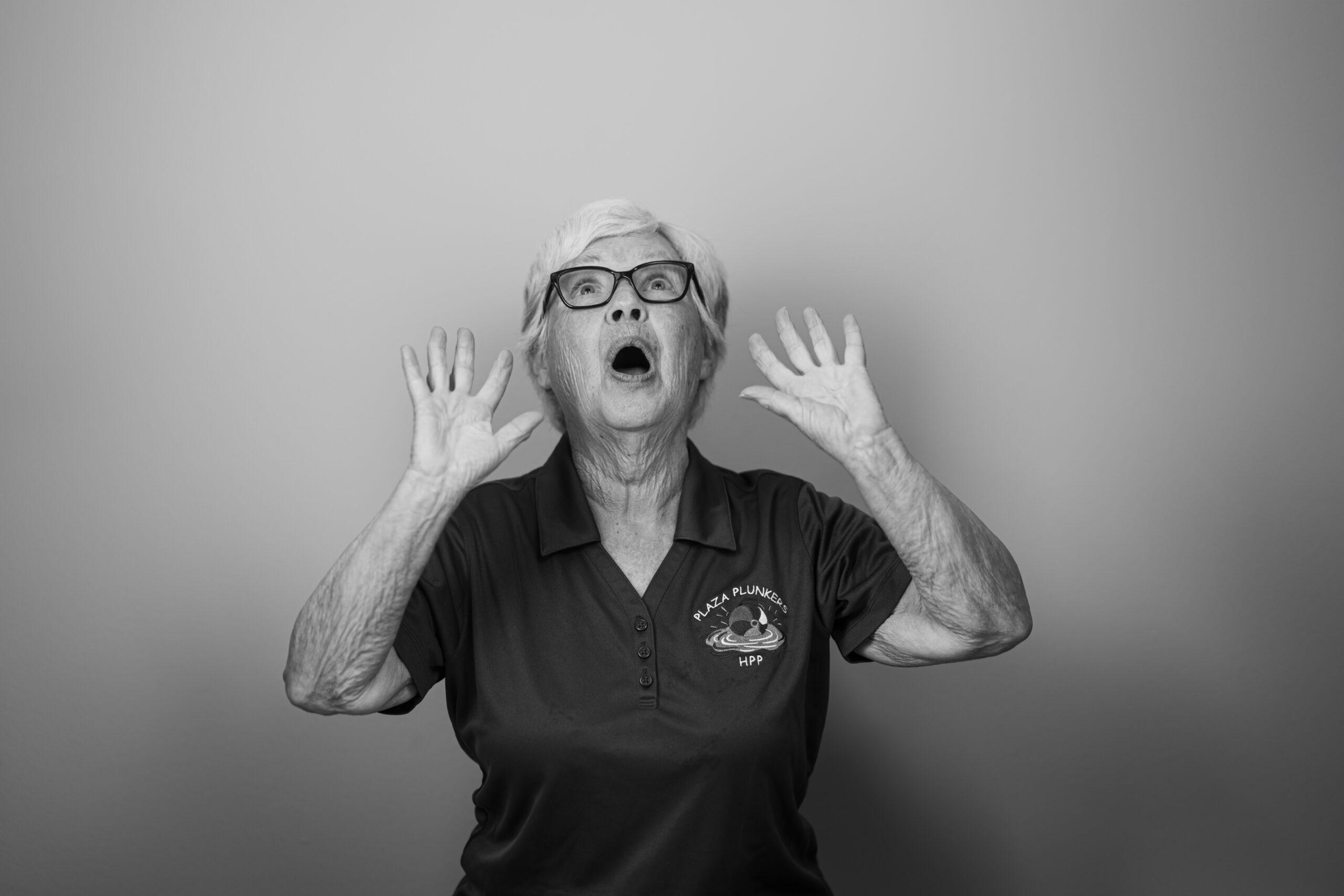 Black and white portrait of a Holladay Park Plaza resident with her mouth open and hands raised to her mouth, as if happily exclaiming or shouting something.