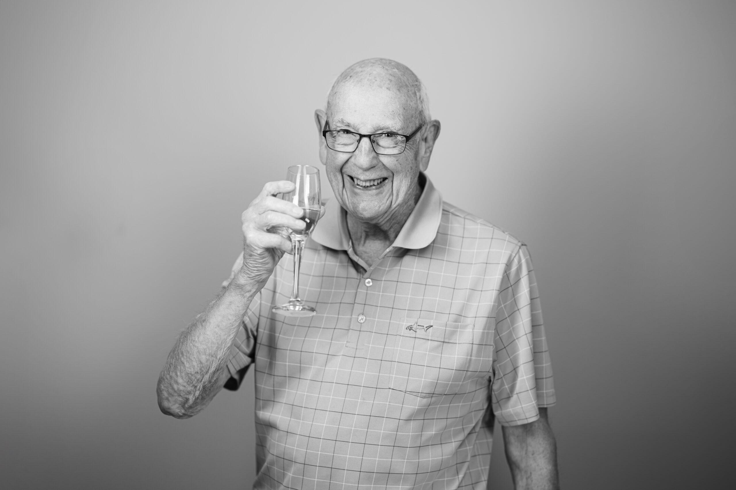 Black and white portrait of a Holladay Park Plaza resident cheerfully holding a glass of champagne.