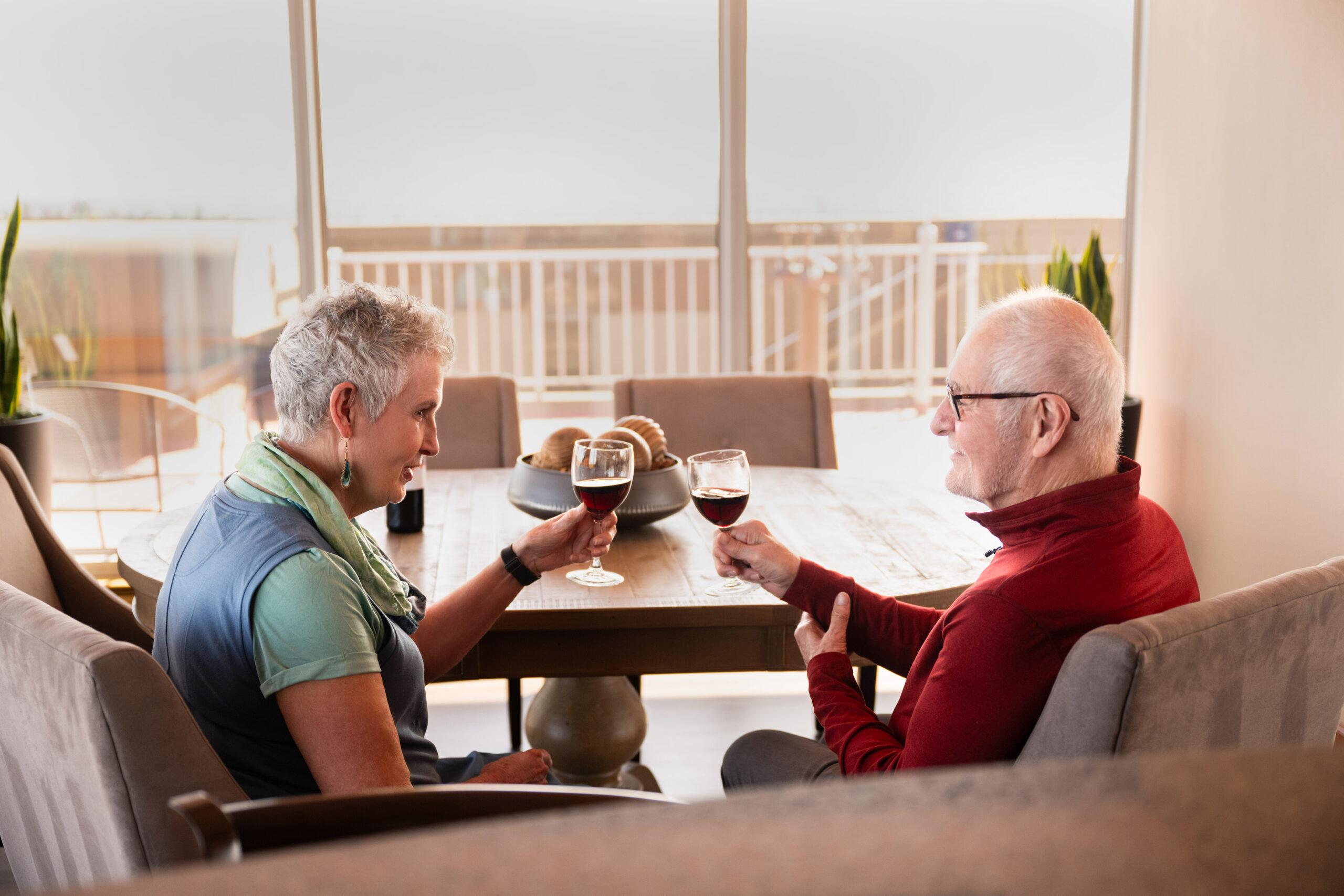 Two Holladay Park Plaza residents cheers wine glasses in an indoor seating area.