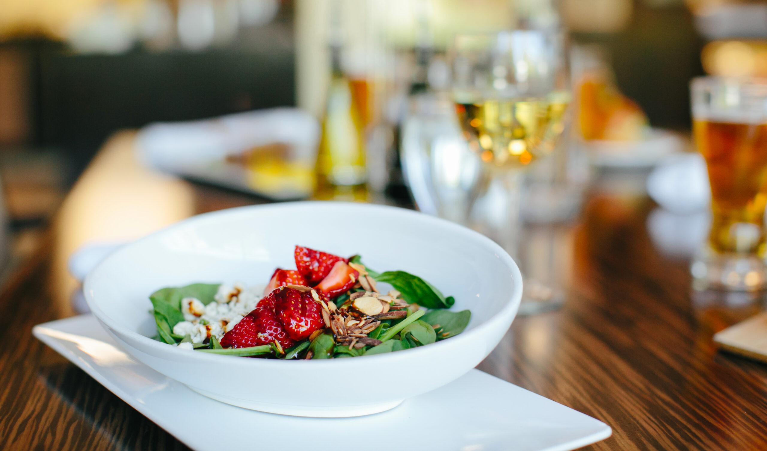 A gourmet salad on a table with glasses of wine in the background.