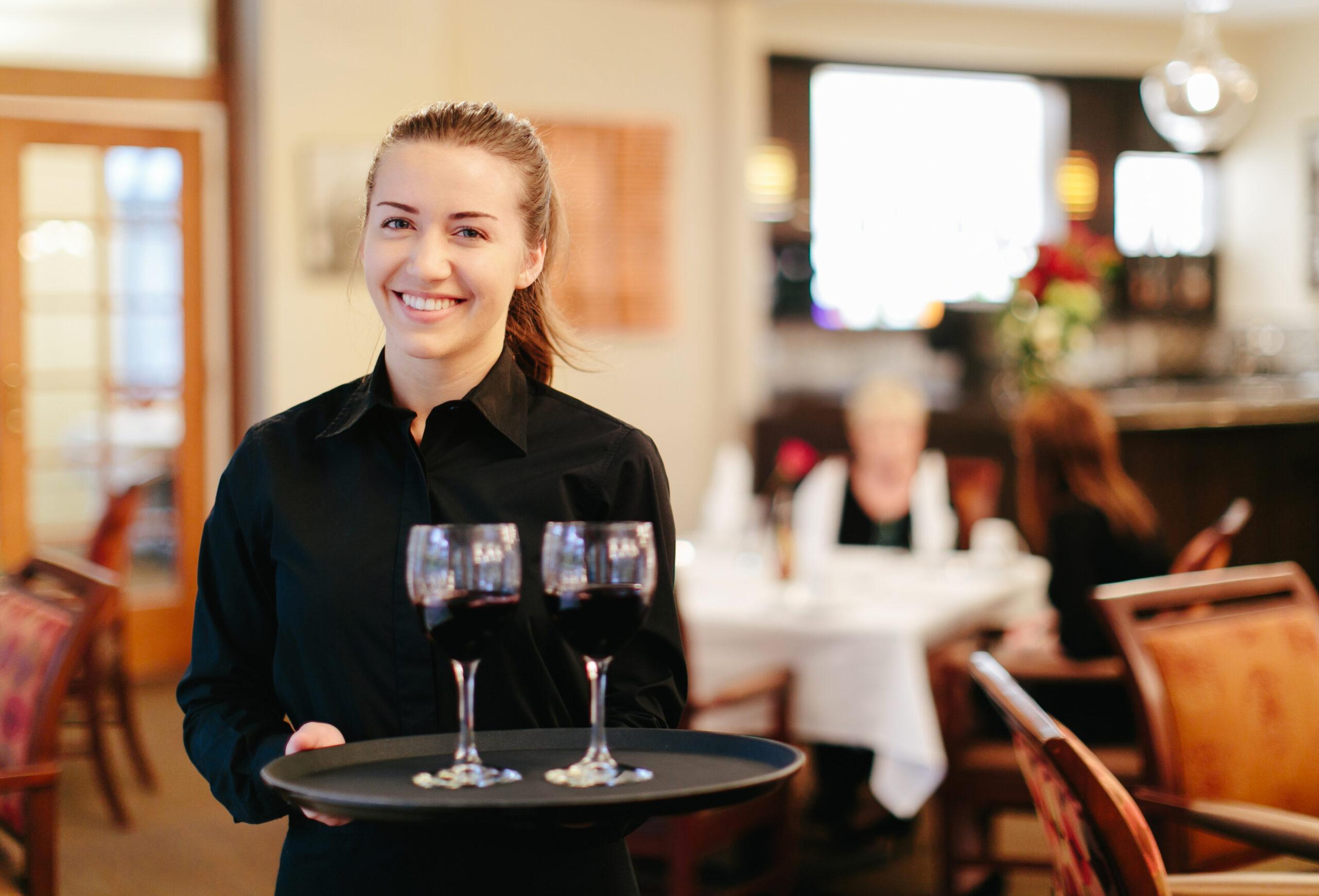 A smiling server holds a tray with wine glasses.