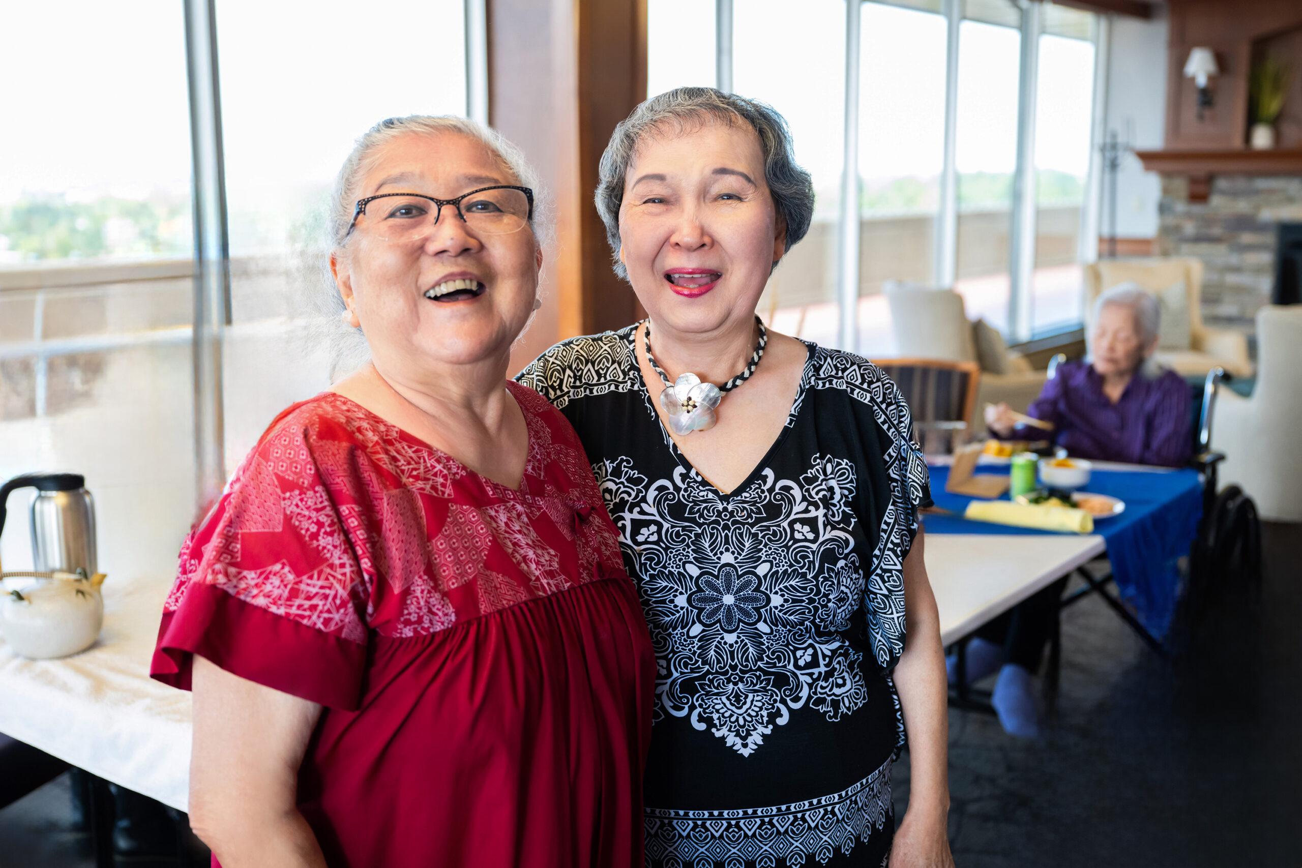 Two friends smile and look at the camera in an indoor gathering space.