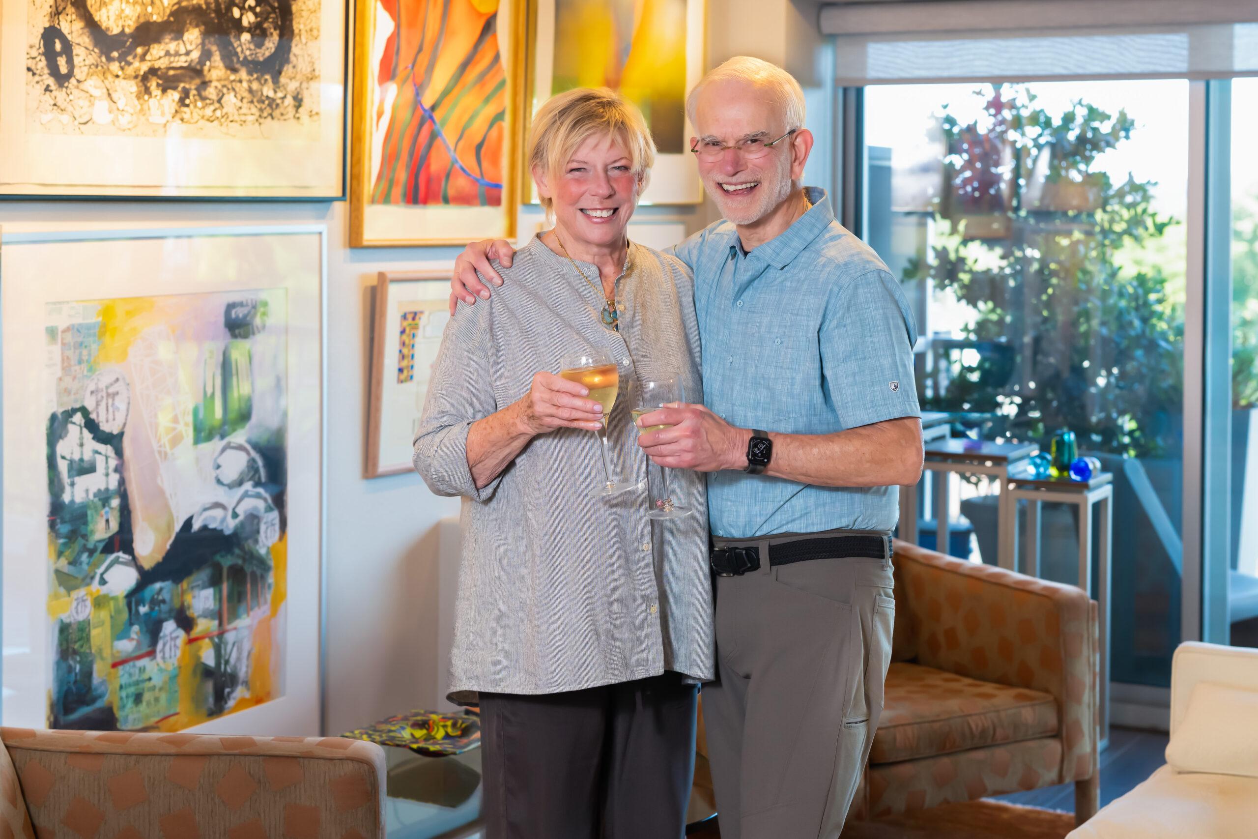 A couple holds wine glasses and smiles for the camera.