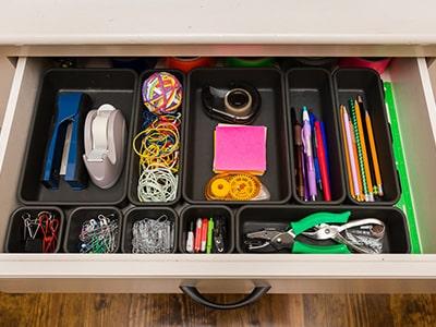 An open drawer full of crafting supplies including pens, pencils, rubber bands, hole punches, clips and more.