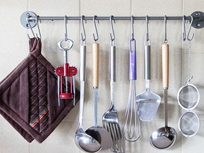 A line of kitchen utensils are hung from a metal bar.